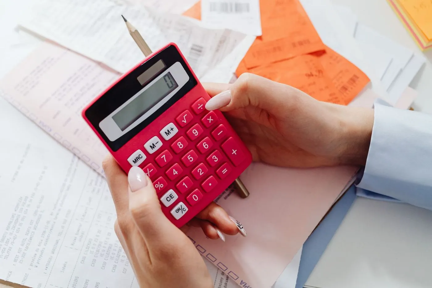 Hands holding a crimson desk calculator over a spread of receipts and printed statements