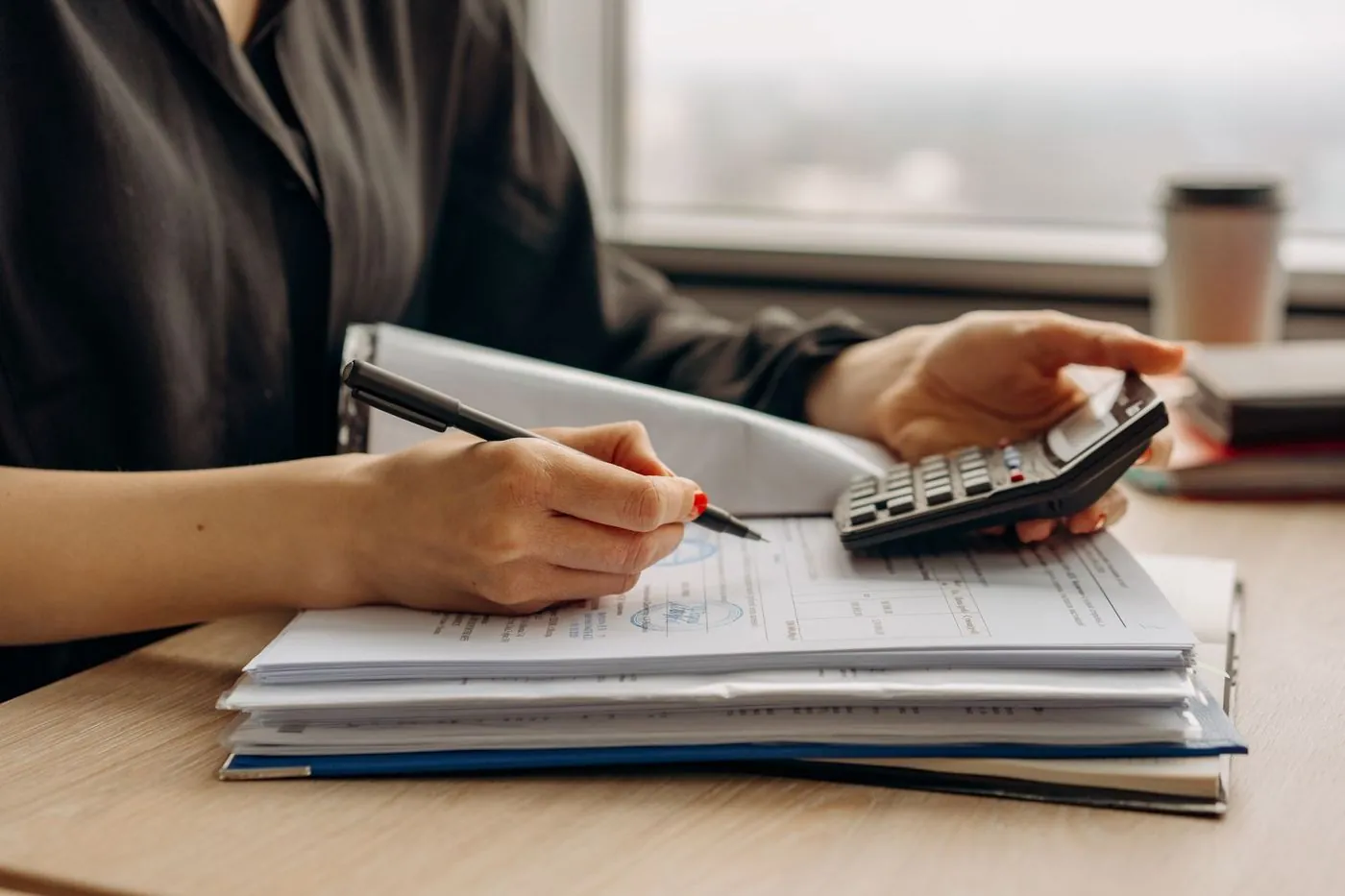A preparer working through a stack of paperwork with a pen in one hand and a calculator in the other