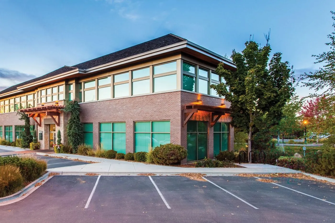 A two-storey brick office building with its own parking lot in a suburban business park at dusk